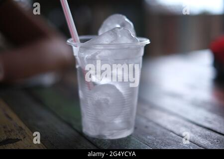 A plastic cup with a straw, full of ice cubes, on a wooden table Stock Photo