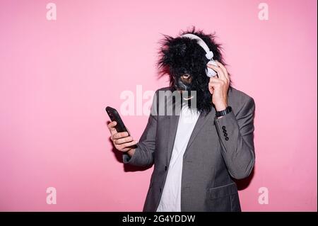 Gesture man with gorilla mask and headphones using smart phone Stock Photo
