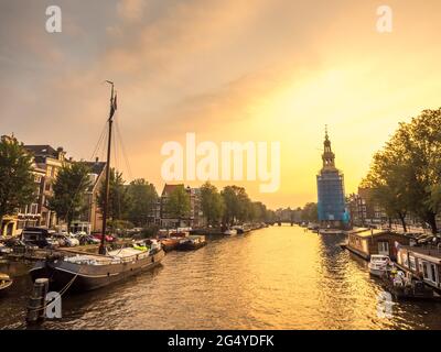 Constructed clock tower along canal in Amsterdam with evening light sky and reflection Stock Photo