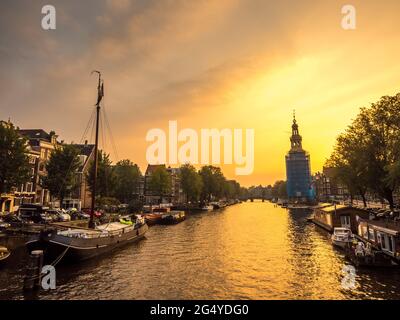 Constructed clock tower along canal in Amsterdam with evening light sky and reflection Stock Photo