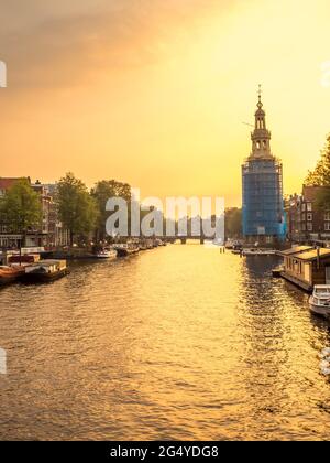 Constructed clock tower along canal in Amsterdam with evening light sky and reflection Stock Photo