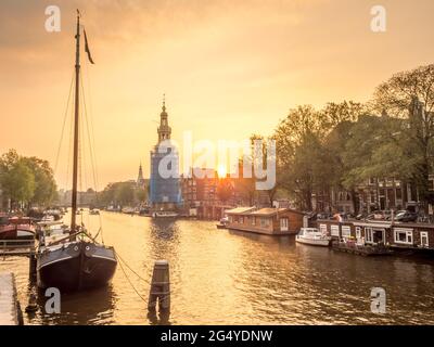 Constructed clock tower along canal in Amsterdam with evening light sky and reflection Stock Photo