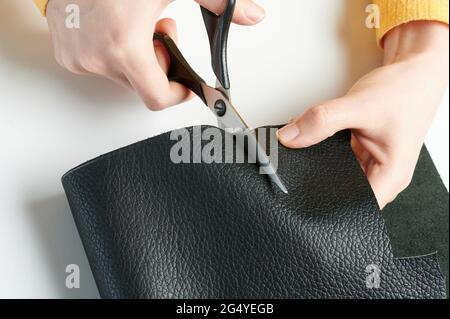 Leather handicraft theme. Woman hands cut black leather piece Stock Photo