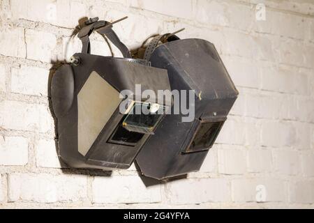 On a white wall hangs two welding masks Stock Photo