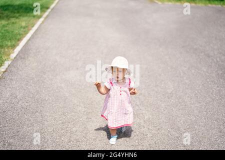 Little girl in dress and hat walks on the asphalt Stock Photo