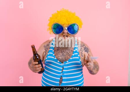 Fat man with beard and wig smokes cigarettes and drinks beer Stock Photo