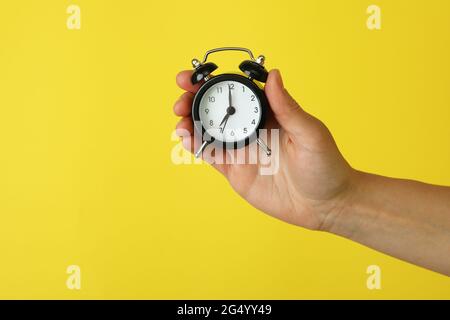Female hand holds alarm clock on yellow background Stock Photo