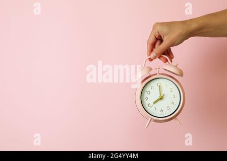 Female hand holds alarm clock on pink background Stock Photo