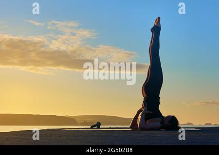 practicing yoga outdoors doing an advanced asana on a pier during a sunrise Stock Photo