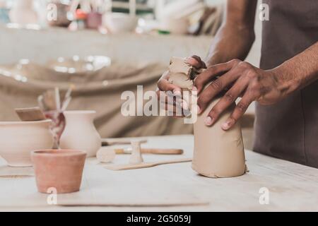 partial view of young african american man working with piece of clay on table with equipment in pottery Stock Photo