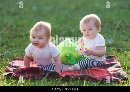 Twin sisters sit on a blanket with backpack of children's toys. Stock Photo