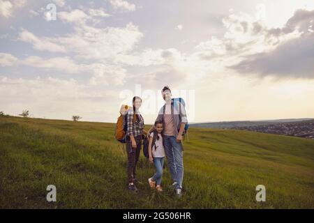 Mother father and girl child with backpacks hiking on the nature track in summer. Stock Photo