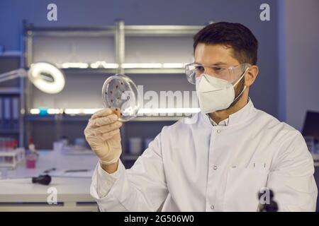 Portrait of a young male scientist in a face mask and goggles holding a Petri dish Stock Photo