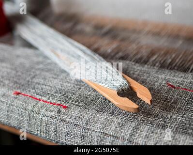 Wooden shuttle with mottled yarn is on the hand weaving loom. Woven grey fabric with red stripes Stock Photo