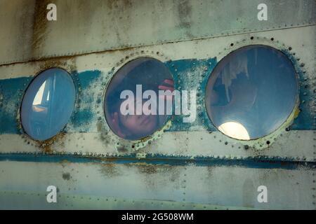 A young man on board an old abandoned Soviet plane. The guy looks out the window. Stock Photo