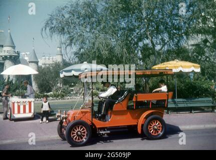 Disneyland, California, 1959. A veteran ‘Disneyland Transportation Co.’ horseless carriage pulls up adjacent to an ice cream vendor. Sleeping Beauty's Castle, Fantasyland and Skyway is in the background. Stock Photo