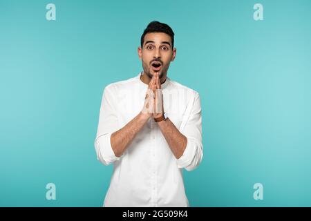 Amazed arabian man with praying hands looking at camera isolated on blue Stock Photo