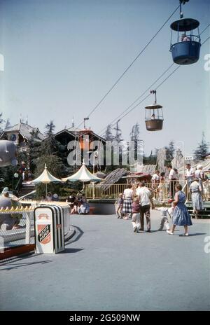 Disneyland, California, 1959. A view of the Swiss Chalet Skyway cable car terminal in Fantasyland. To the left is the Dumbo Flying Elephants ride and right is the exit for the Casey Jr. Circus Train. Visitors are passing by and taking shelter from the sun under parasols. Stock Photo