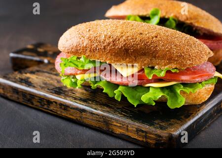 Healthy sandwiches with bran bread, cheese, lettuce, tomato and sliced salami on a rustic wooden stand. Breakfast concept. Top view. Stock Photo