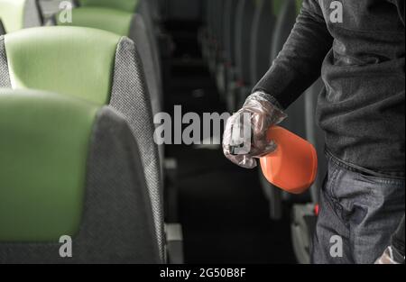 Coach Bus Driver Cleaning and Disinfecting Vehicle Seat Armrests Wearing Vinyl Gloves. Public Transportation and Pandemic Theme. Stock Photo