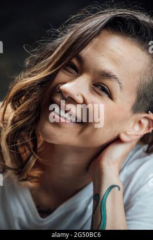 A portrait of a young woman smiling and leaning her head on her hand while looking at the camera. Stock Photo