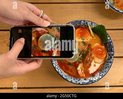 woman taking photo of bowl of Tom Yum Kung noodle on her smartphone to share on social networks. Tom Yum Kung is the Thai popular food Stock Photo