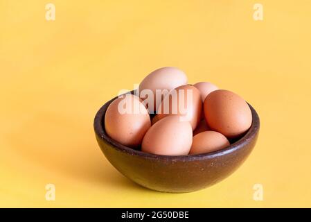 Eggs on a brown rustic artesanal bowl with yellow background Stock Photo
