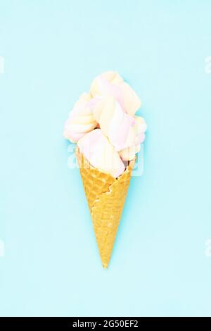 Colorful marshmallow candy in an ice cream cone on a blue background. Flat lay, copy space, vertical. Stock Photo