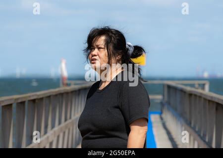 An Asian middle aged woman on a jetty with a blue ocean and sky in the background. Picture from Scania county, Sweden Stock Photo