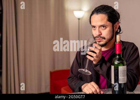 Young latin man drinking red wine at home in the living room Stock Photo