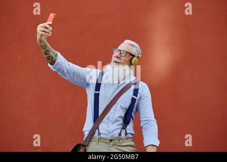 Smiling elderly man taking selfie on smartphone on red background Stock Photo