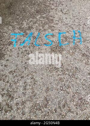 German text „FALSCH“ (wrong) painted on asphalt road surface with vibrant bright blue paint. Concrete ground background with copy space, vertical Stock Photo