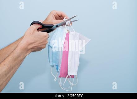 Hands cutting a group of masks with scissors on a blue background. COVID-19. Stock Photo