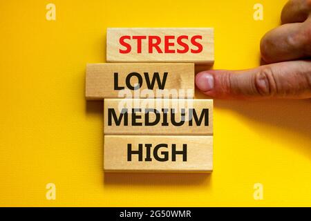 Low or high stress level symbol. Businessman chooses the wooden block with words low stress. Words stress low medium high. Beautiful yellow background Stock Photo