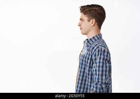 Profile portrait of young caucasian guy, boy with hairstyle and clean side of face, smiling and looking aside at empty space left, standing against Stock Photo