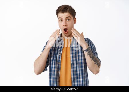 Image of shocked man drop jaw, say wow and stare startled, look in awe, holds hands near face, cant belive something, standing in disbelief against Stock Photo