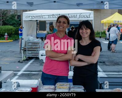 Reston, VA, USA -- June 5, 2021. Two women pose behind their food stand at the Reston Farmers Market on a summer morning. Stock Photo