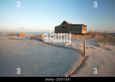 Abandoned beach shack on the Atlantic Ocean coast with sand dunes and a wooden fence. Stock Photo