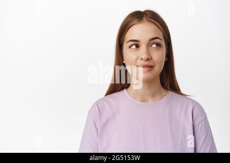 Hmm tasty. Young woman biting lip from temptation, thinking of smth delicious or tempting, looking aside thoughtful, standing in t-shirt against white Stock Photo