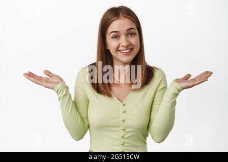 Sorry cant help you. Unbothered smiling girl shrugging shoulders unaware, being clueless, dont know and not care, standing against white background Stock Photo