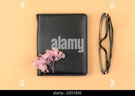 Minimal workspace concept with black leather notebook, pink dried flower and glasses, top view composition Stock Photo