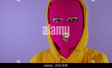 Unrecognizable woman in pink balaclava smiles on purple background