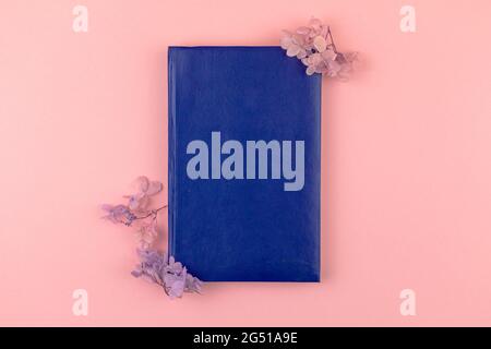 Empty blue leather notepad notebook mockup with dried flower border composition, pink background, top view Stock Photo