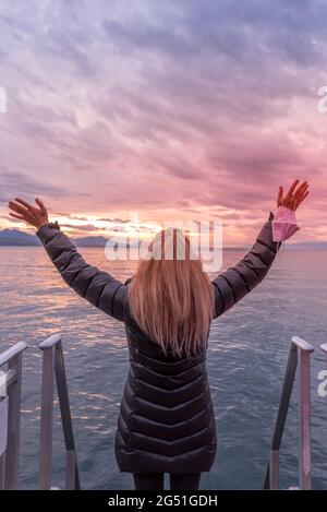 Faceless blonde woman in the coast raising her arms and holding her face mask. Vertical photo Stock Photo