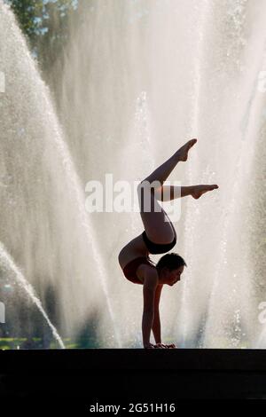 Silhouette of woman doing acrobatic handstand pose against fountain Stock Photo