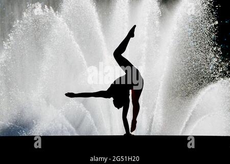 Silhouette of woman doing acrobatic handstand pose against fountain Stock Photo