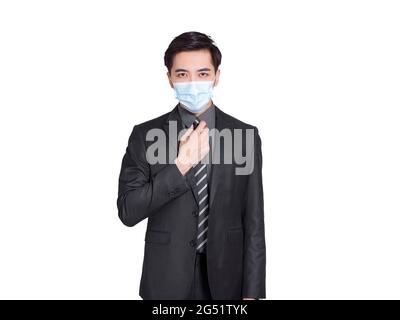 young businessman wearing  medical mask during the COVID-19 pandemic, confidently adjusts his tie in front of the camera Stock Photo