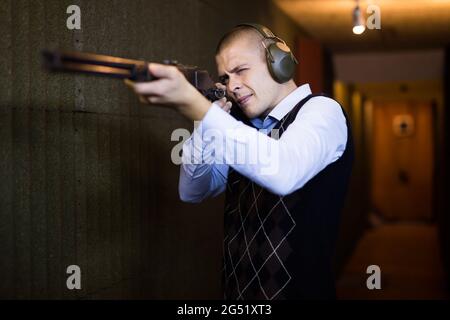 Concentrated man practicing shotgun shooting at firing range Stock Photo