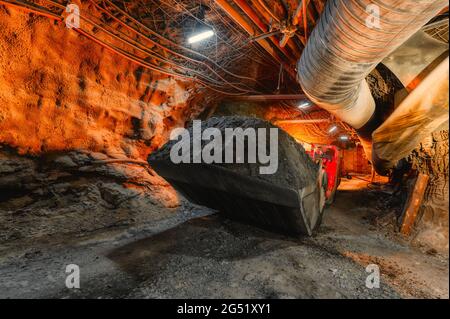 An underground loading machine carries a full bucket of ore. Special low-profile equipment for underground work Stock Photo