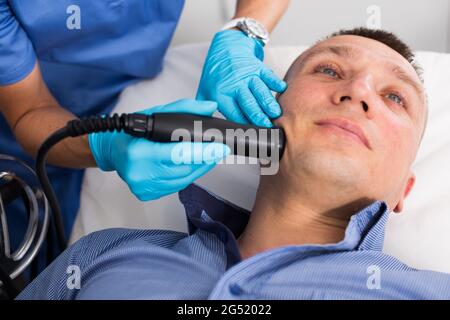 Woman doctor is doing vacuum massage procedure on face of adult client Stock Photo